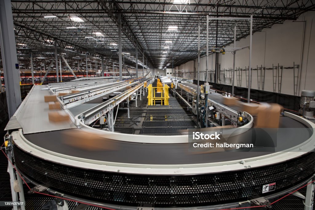 Long Exposure of Packages on Conveyor Belt Packages blur as they rush past on the complex conveyor belt system that sorts them for delivery at a large fulfillment center. Conveyor Belt Stock Photo