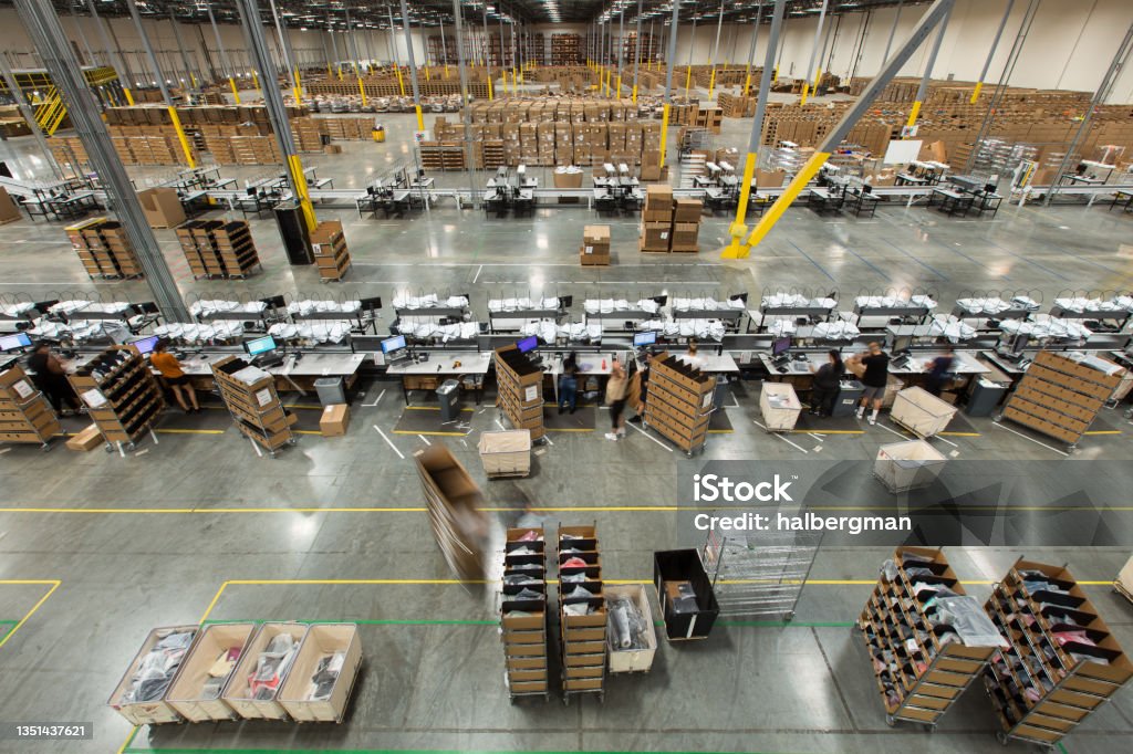 Packing Stations in Fulfillment Center High angle view of lines of packing stations in a fulfillment center.  A team of packers are packaging up orders brought to them on carts from the picking area, then throwing them onto a conveyor belt. Warehouse Stock Photo
