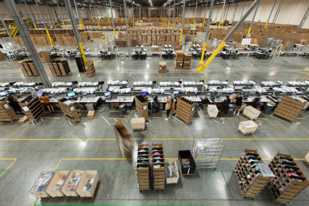 Packing Stations in Fulfillment Center High angle view of lines of packing stations in a fulfillment center.  A team of packers are packaging up orders brought to them on carts from the picking area, then throwing them onto a conveyor belt. distribution warehouse stock pictures, royalty-free photos & images