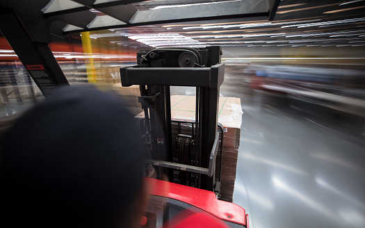 Long exposure shot over the shoulder of a warehouse worker taken from a camera mounted on a forklift moving around a massive fulfillment center.