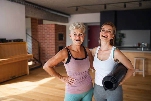 happz mujer mayor activa después del entrenamiento con su hija en el interior de su casa, mirando a la cámara - senior adult relaxation exercise healthy lifestyle exercising fotografías e imágenes de stock