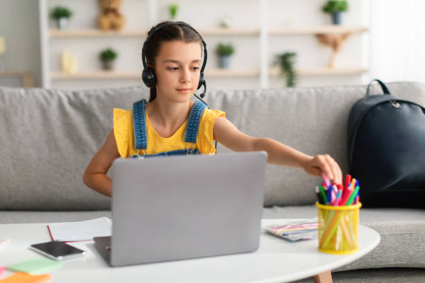 istock Girl in headset using laptop, taking pen from pencil holder 1351439439