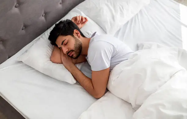 Photo of Asleep young arab man sleeping, resting peacefully in comfortable bed, lying with closed eyes, free space