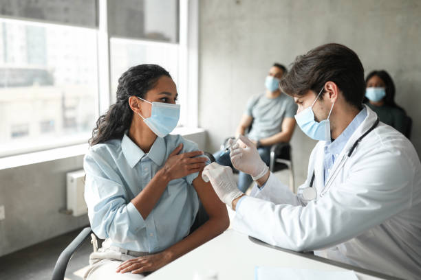 istock Female patient looking at handsome doctor while getting vaccination 1351440311