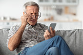 Senior Man Squinting Eyes Reading Message Wearing Eyeglasses At Home