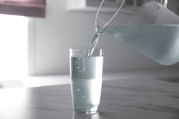 istock Pouring water from jug into glass on white marble table in kitchen 1351442566