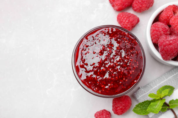 istock Delicious jam and fresh raspberries on white table, flat lay. Space for text 1351442579