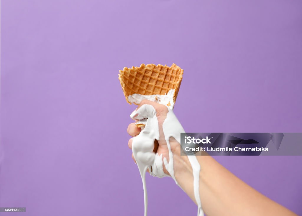 Woman holding crushed wafer cone with molten ice cream on violet background, closeup Ice Cream Stock Photo