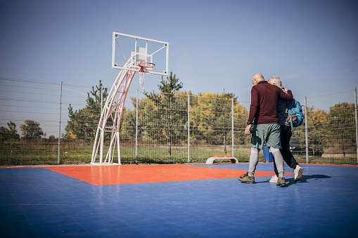 Two men, senior men arriving on basketball court to play one on one outdoors.