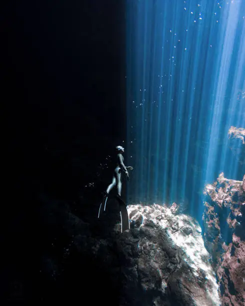 A Japanese Freediver glides between the sunlight and the darkness of a Mexican Cenote