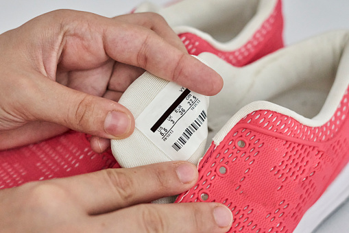 A person cleans and cares for tennis and athletic shoes. Woman checking care label on shoes. Female reading the label of pink sport shoes before putting into automatic washing machine