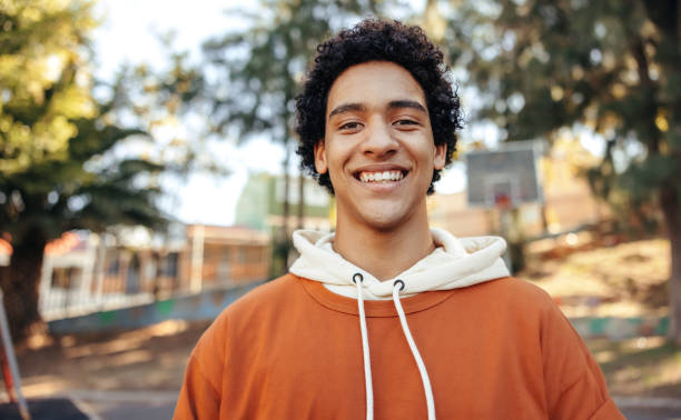 Happy male youngster smiling at the camera outdoors Happy male youngster smiling at the camera outdoors. Fashionable teenager wearing casual clothing in an urban park. Cheerful teenage boy standing alone during the day. teenagers only stock pictures, royalty-free photos & images