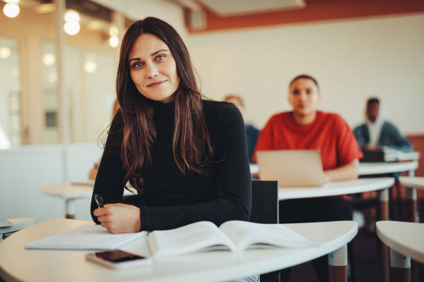 Beautiful student in university classroom Portrait of a beautiful female student in classroom. High school sitting in a lecture looking at camera. community college stock pictures, royalty-free photos & images