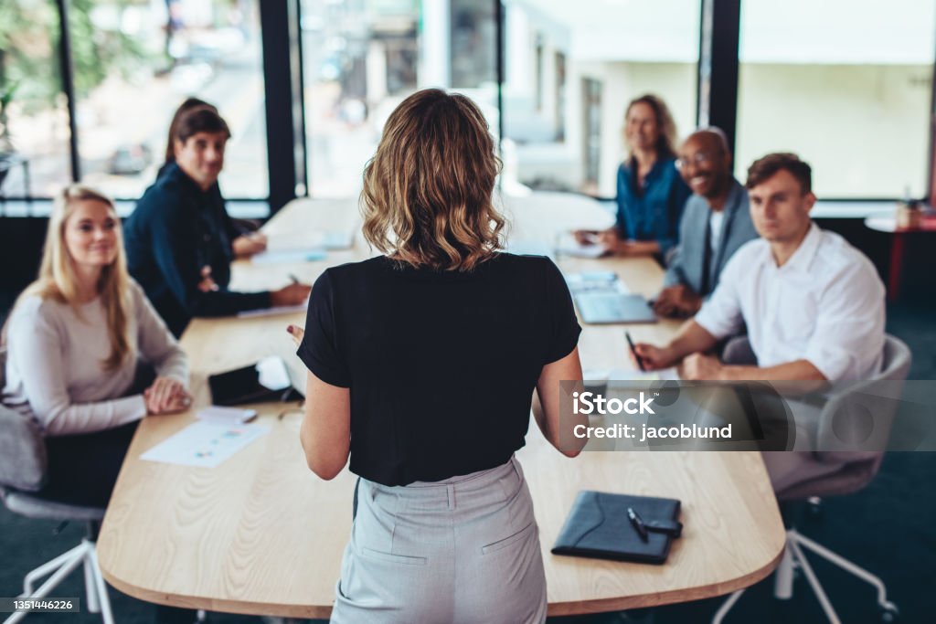 Businesswoman addressing a meeting in office Rear view of a businesswoman addressing a meeting in office. Female manager having a meeting with her team in office boardroom. Leadership Stock Photo