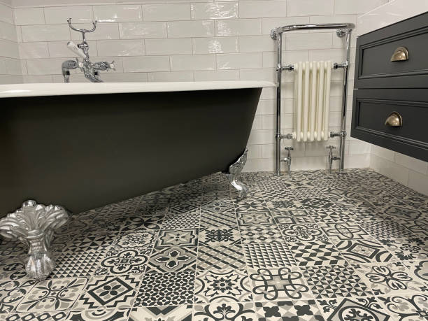 Close-up image of luxury bathroom suite with Victorian style, white ceramic freestanding curved roll top bath with metal claw feet, chrome, bath shower mixer tap, wall mounted vanity unit, black and white patterned floor tiles stock photo
