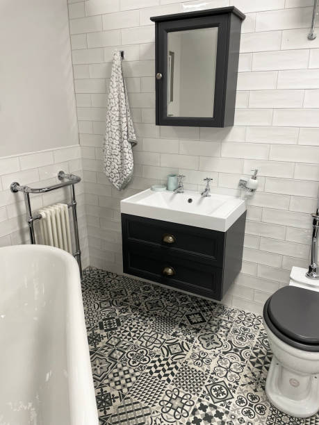 istock Image of luxury bathroom suite with Victorian style, white ceramic freestanding curved roll top bath with metal claw feet, chrome, bath shower mixer tap, wall mounted vanity unit topped by sink, toilet with wood toilet lid, black and white pattern 1351446290