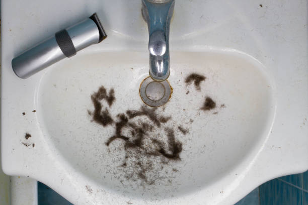 грязная раковина в ванной комнате с волосами после бритья и беспроводная электрическая бритва.  свежестриженые волосы с головы, бороды и ус - shaving equipment wash bowl bathroom razor стоковые фото и изображения