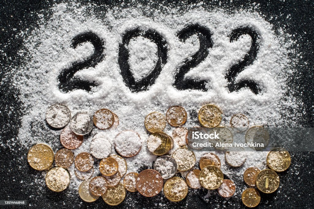 Hand written year 2022 and various coins covered with white sea salt such as snow on black background New year concept - close-up of hand written year 2022 and various coins covered with white sea salt such as snow on black background, selective focus. New Year card. The concept of wealth and success 2022 Stock Photo