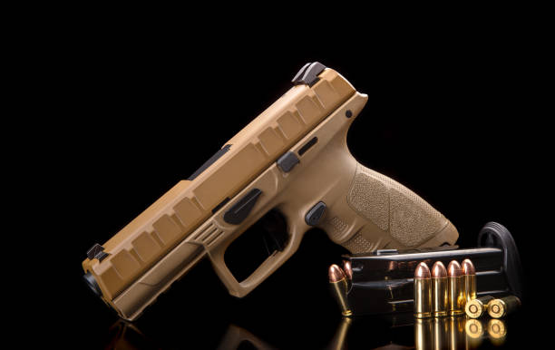 istock Brown modern gun and ammunition for it on a dark reflective surface. Short-barreled weapons for sports and self-defense. Armament for police units, special forces and the army. Black background 1351447994