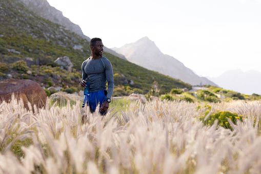 Portrait of fit african american man in sportswear standing in tall grass, looking in the distance. healthy lifestyle, exercising in nature.