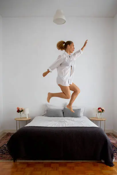 Woman jumping with joy over her bed