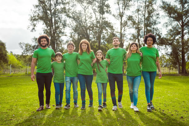 Volunteers at park during environmental cleanup Portrait of smiling male and female volunteers at park. Environmentalist are walking with arms around. They are in green t-shirts. walking for a cause stock pictures, royalty-free photos & images