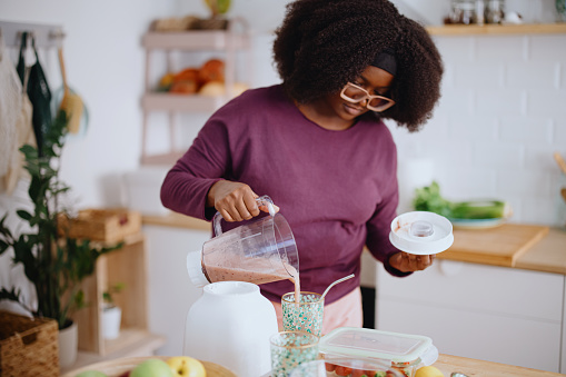 Young black woman preparing healthy smoothie in her kitchen. Woman slicing fresh organic fruits for smoothie in her kitchen.