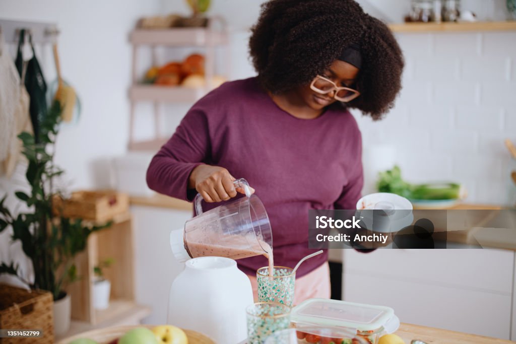 Woman preparing fresh fruit smoothie Young black woman preparing healthy smoothie in her kitchen. Woman slicing fresh organic fruits for smoothie in her kitchen. Smoothie Stock Photo