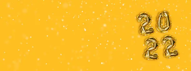 2022 golden foil balloons decor and Christmas snow with copy space on a yellow background. New Year concept