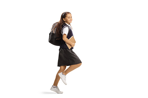 Girl in a school uniform with a backpack hopping to school isolated on white background