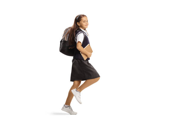 full length profile shot of a girl in a school uniform with a backpack hopping to school - full hair imagens e fotografias de stock