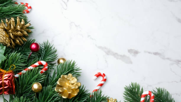 istock Green pine tree leaves, red christmas decorations and candy canes on white marble background, christmas decorations in bright red color. Simple and creative christmas concept. 1351459507