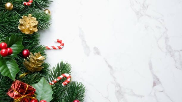 istock Green pine tree leaves, red christmas decorations and candy canes on white marble background, christmas decorations in bright red color. Simple and creative christmas concept. 1351459895