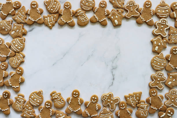 Stock photo showing a Christmas poster border design with homemade cut out baubles, Christmas trees, houses, snowmen and gingerbread men cookies iced with white glace icing on marble effect background, with copy space.