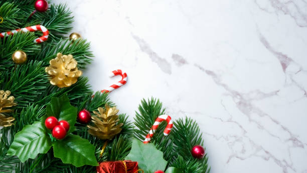 istock Green pine tree leaves, red christmas decorations and candy canes on white marble background, christmas decorations in bright red color. Simple and creative christmas concept. 1351460485