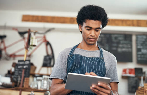 istock Shot of a young male waiter using a digital tablet at a cafe 1351461027
