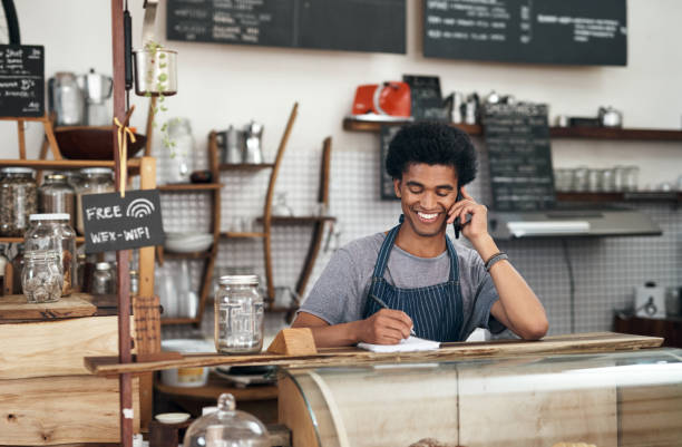 istock Shot of a young male waiter using a notebook while on a call at a cafe 1351461075