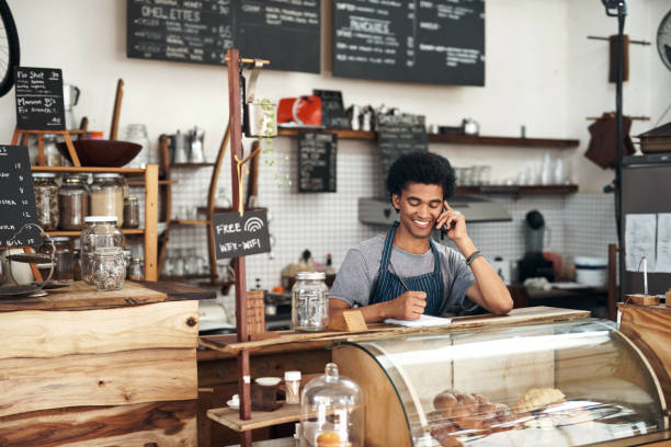 istock Shot of a young male waiter using a notebook while on a call at a cafe 1351461086