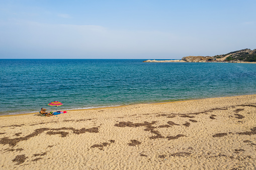 Sithonia, Greece - September 13, 2021: Man lies on sun chair on the beach with colourful sun umbrella