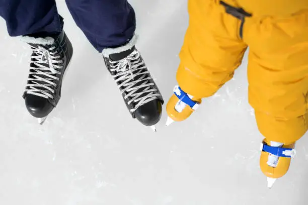 Photo of Skates of a child and a man on an ice rink. Ice skating lessons