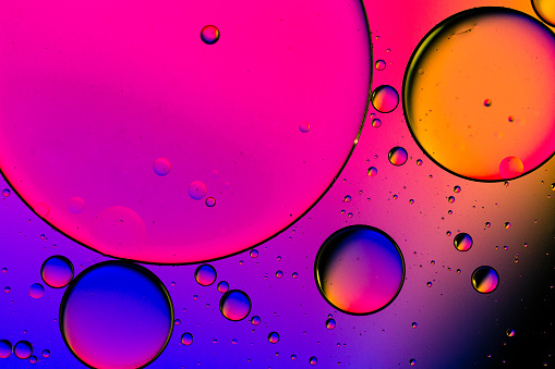 Close up macro image depicting droplets of oil in water on a multi colored background. The oil forms interesting circles and spheres in the water, and colorful background produces an abstract effect.