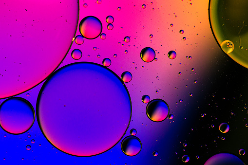 Close up macro image depicting droplets of oil in water on a multi colored background. The oil forms interesting circles and spheres in the water, and colorful background produces an abstract effect.