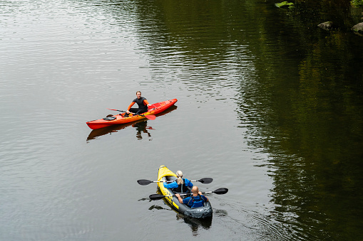 Elevated view of a mid adult couple kayaking on a river in Warkworth, Northumberland. They are approaching a young man in a kayak, who is telling them to stop to avoid them crashing into him on the river.