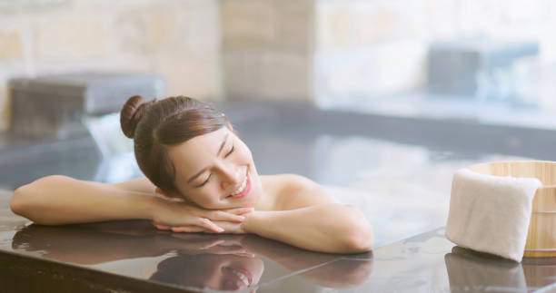 smiling asian young woman lying on the bathtub with crossed arms is relaxing in hot spring