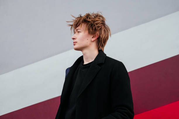 istock Thinking young man with birthmarks, moles, wart on face in black coat standing in front of colorful wall on a city street and looking away. Handsome man waiting for someone. Breathing fresh air. 1351472567