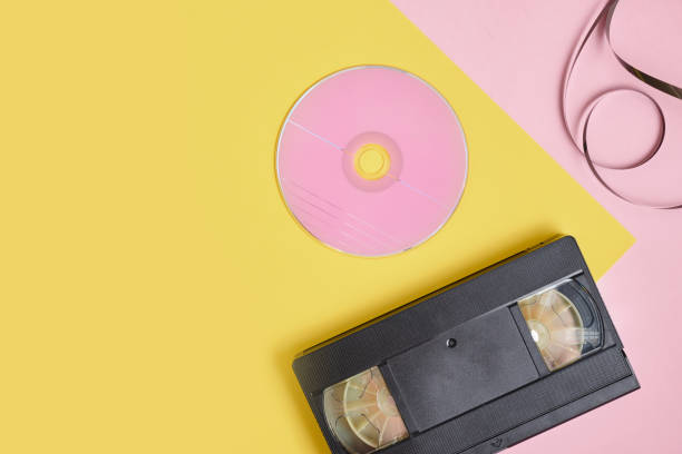 cd disc and videotape on pink and yellow background, vintage video cassette and compact disc with pink label copy space - dvd obsolete cd cd rom imagens e fotografias de stock