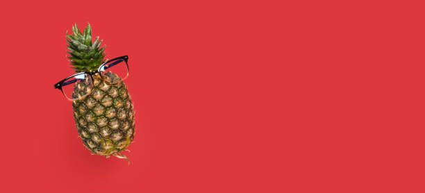 levitating pineapple with glasses on a red background copy space