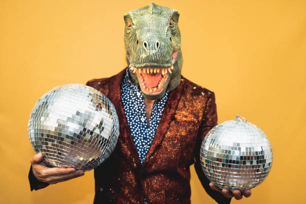 Fashion senior man wearing t-rex dinosaur mask while celebrating carnival holidays - Surreal masking concept stock photo