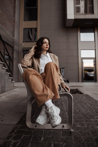 Chica alta y elegante con chaqueta de gran tamaño sentada en el banco del fondo de la ciudad photo