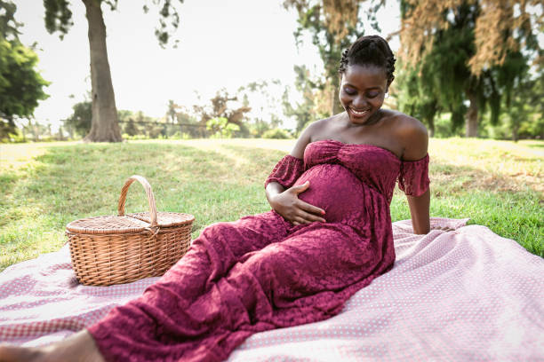 african woman caressing her pregnant belly while doing a picnic in park - maternity lifestyle concept - nature human pregnancy color image photography imagens e fotografias de stock
